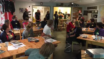 Personer sittandes runt bord inomhus i en klubbstuga